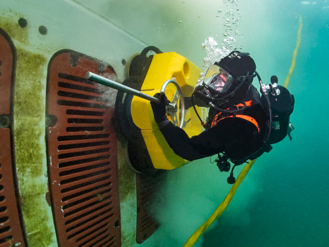 Underwater view of a vessel hull, propeller and rudder during cleaning